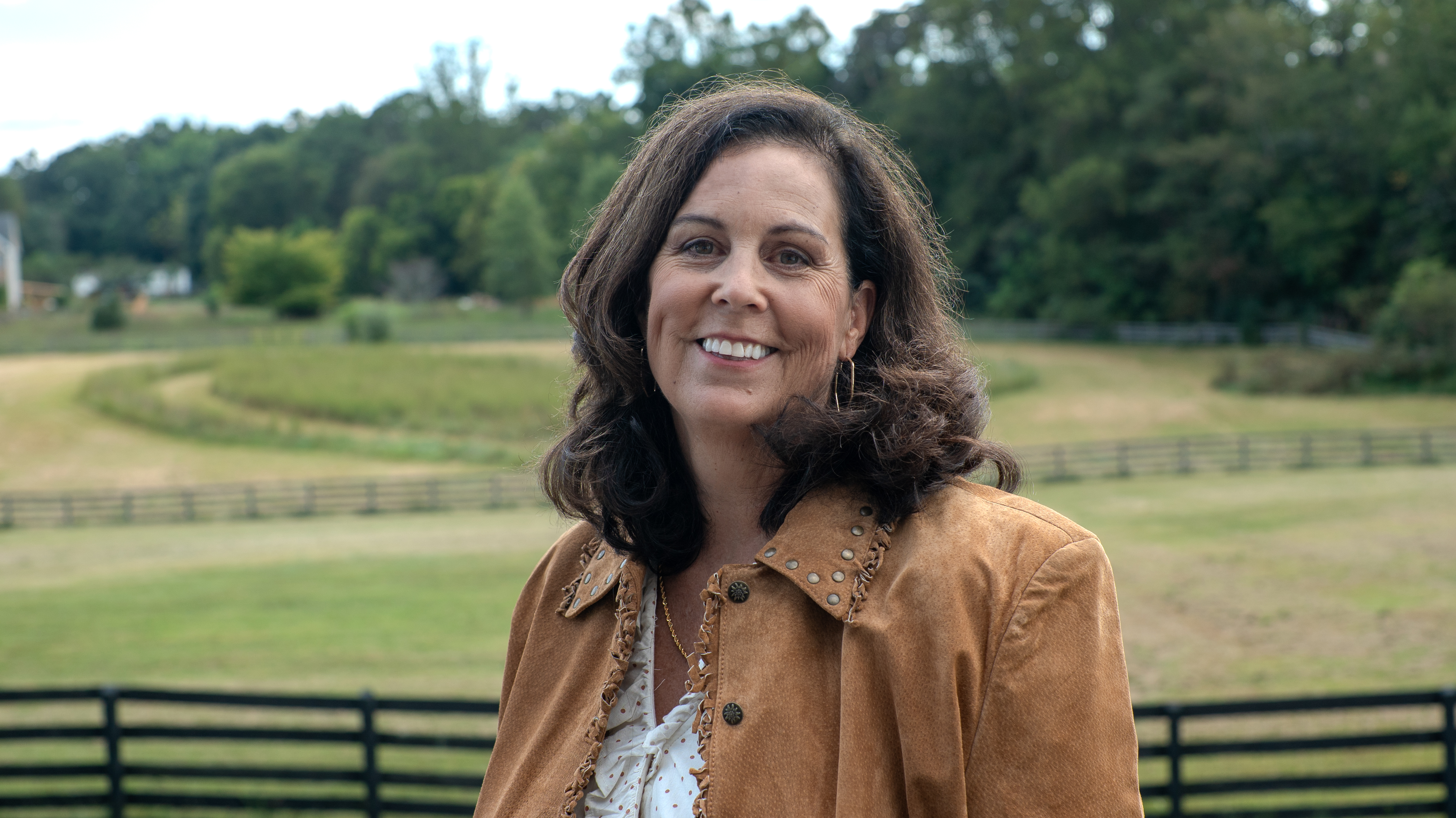 Carolyn Freudenthal on her deck with the pasture and fences behind her
