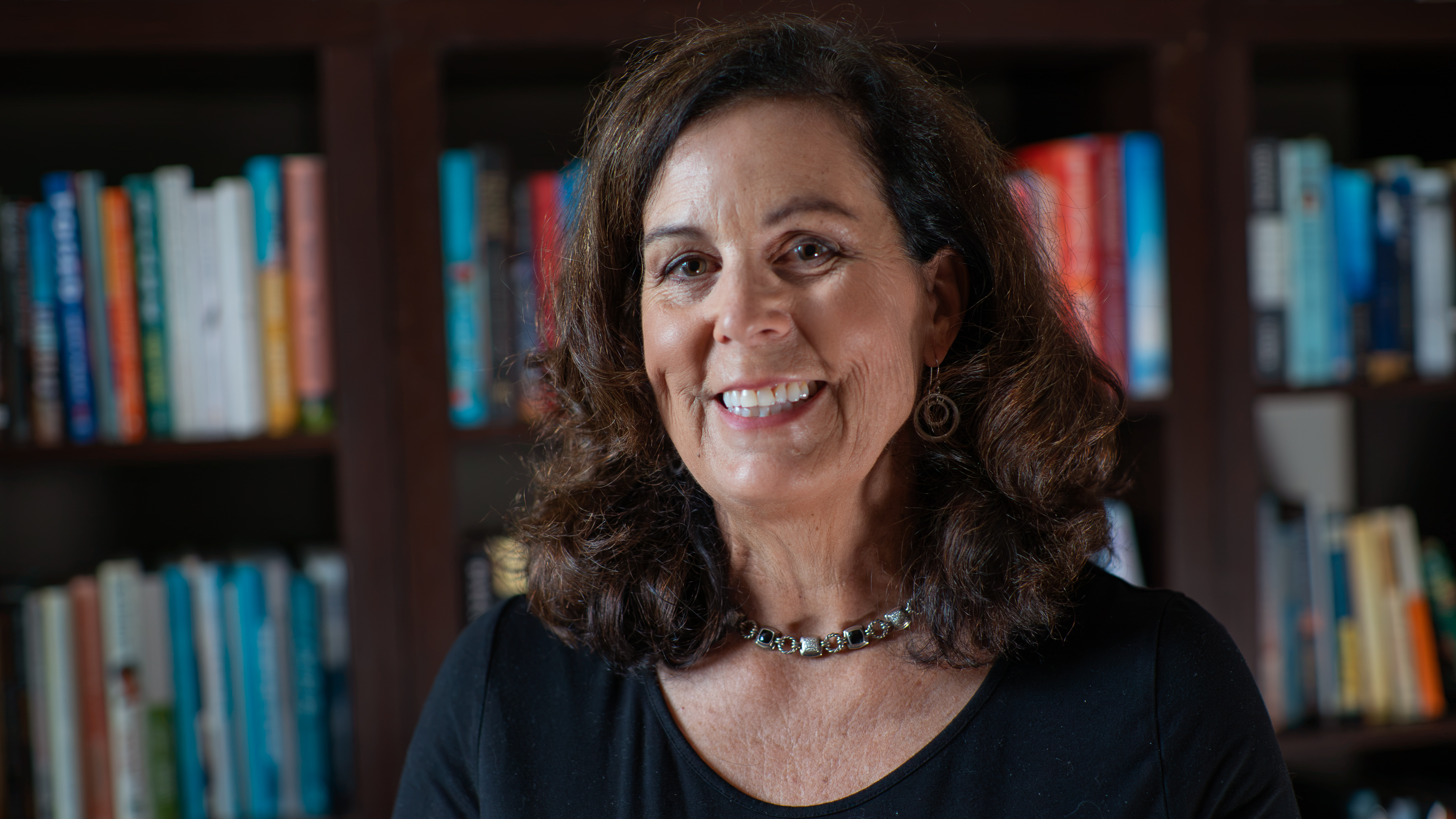 Carolyn Freudenthal smiling in front of a bookcase filled with books