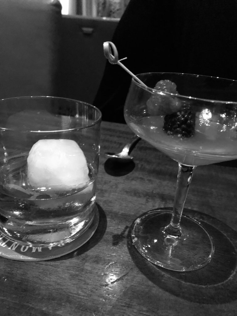 Black and white photograph of two cocktails on a bar table