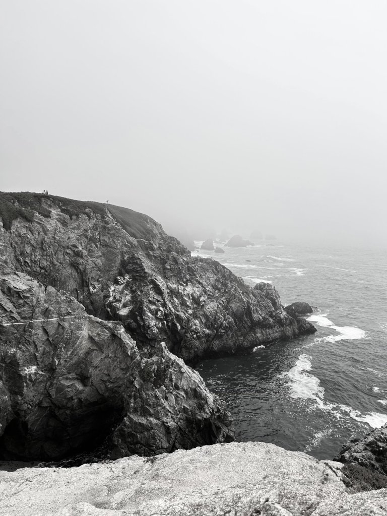 Black and white photograph of a foggy rocky cliff meeting the ocean
